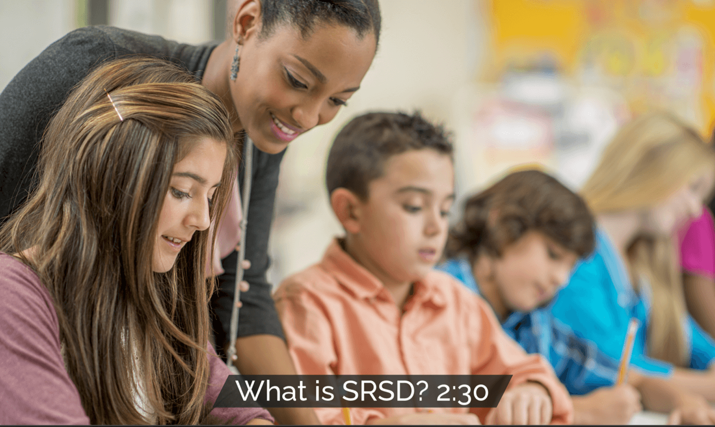 A teacher helping students in a classroom, illustrating the explicit and systematic approach of SRSD.