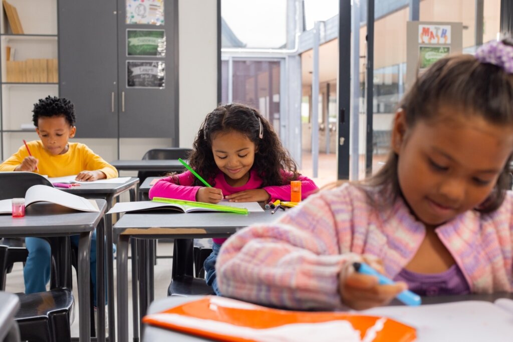 Young students engaged in classroom activities, writing and drawing in their notebooks.