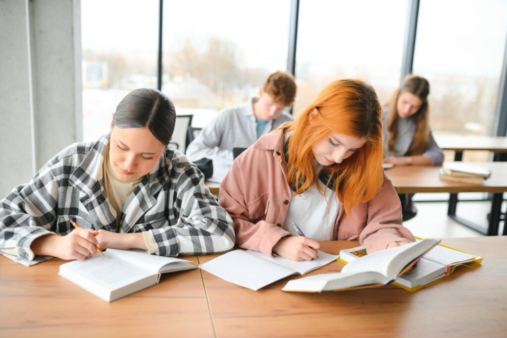 Students studying in a modern classroom with focus on two young women taking notes and reading books.