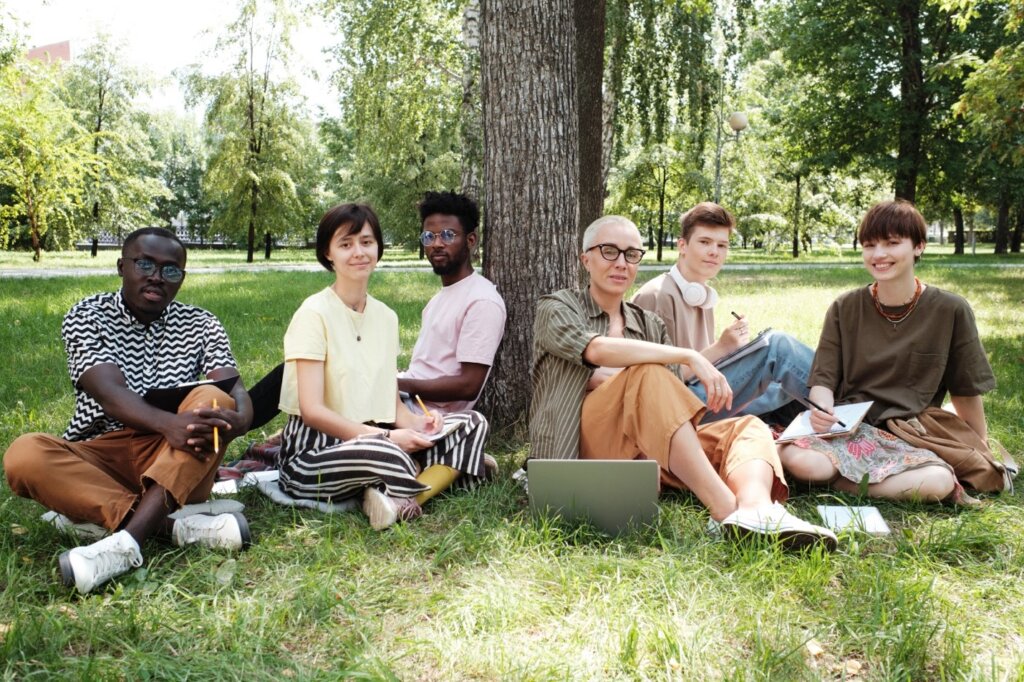 A diverse group of students studying outdoors, sitting on the grass under a tree in a park.