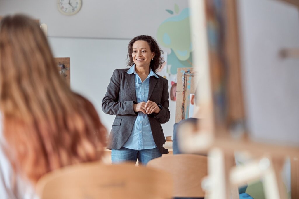 A smiling teacher engaging with students in an art classroom, fostering creativity and confidence.