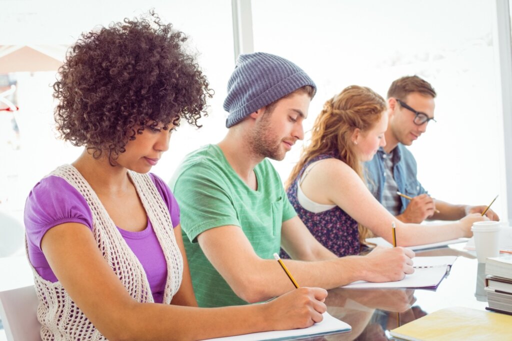 A diverse group of young adults writing in notebooks during a collaborative learning session in a bright, modern setting.