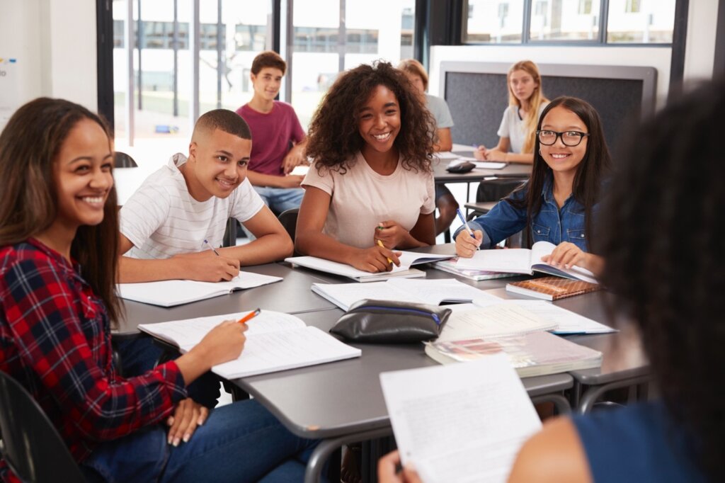 A group of high school students smiling and participating in a classroom discussion while taking notes.