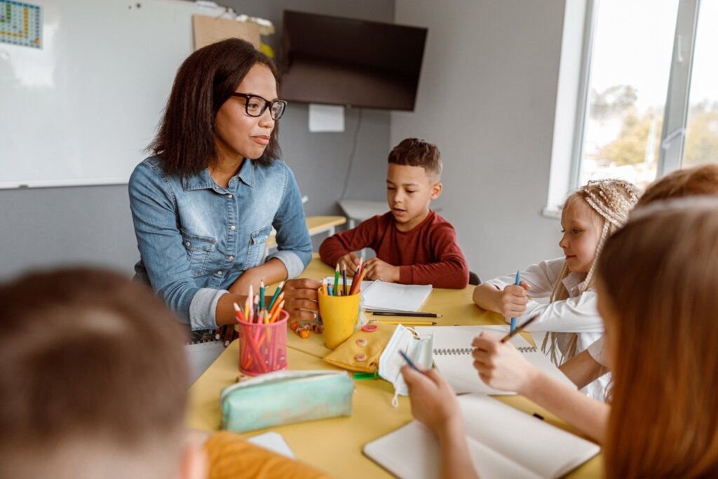 Teacher guiding a small group of elementary students during a writing activity at a classroom table