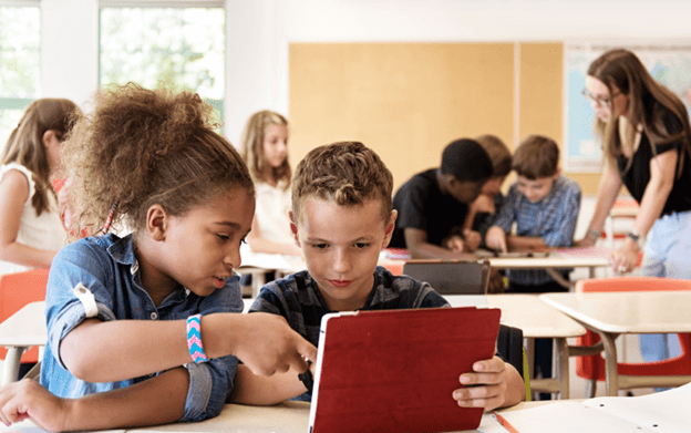 Elementary students collaborating on a digital tablet in a bright classroom.