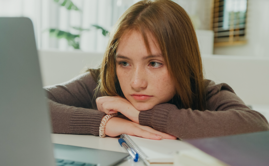 Student looks disengaged and bored while staring at laptop during remote learning.