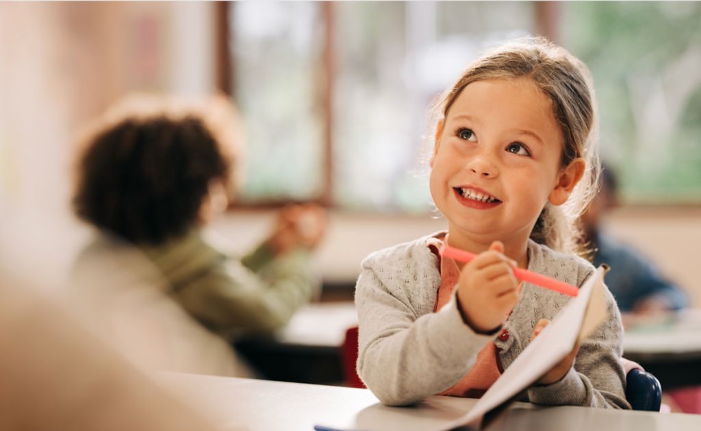 Kindergarten student smiling while writing in notebook during structured SRSD writing instruction.