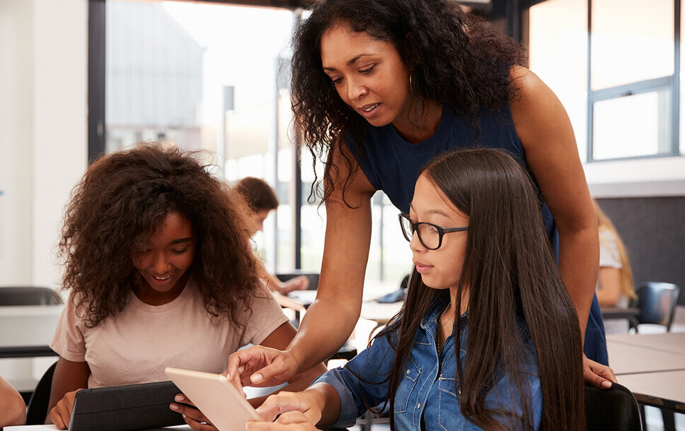 Teacher helping two students with a tablet