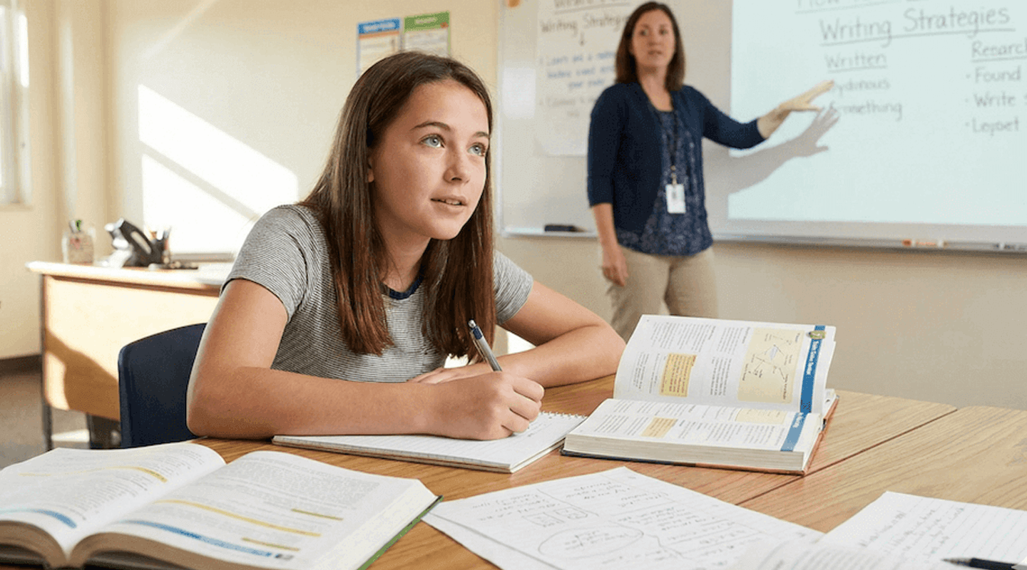 Student listening as a teacher points to writing strategies on the whiteboard
