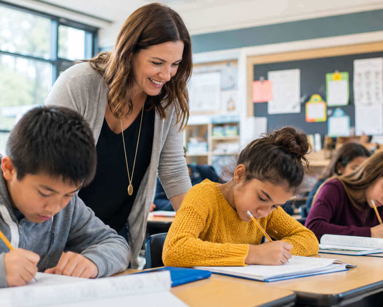 Teacher checking student work while students write at their desks